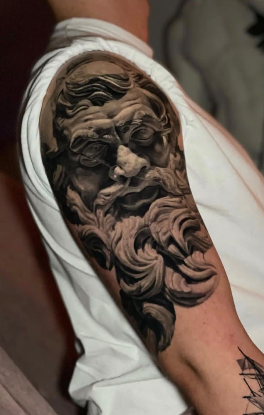 Realistisches Statuen-Tattoo eines bärtigen Gottes auf dem Oberarm von Andrei Tiron Eckernförde